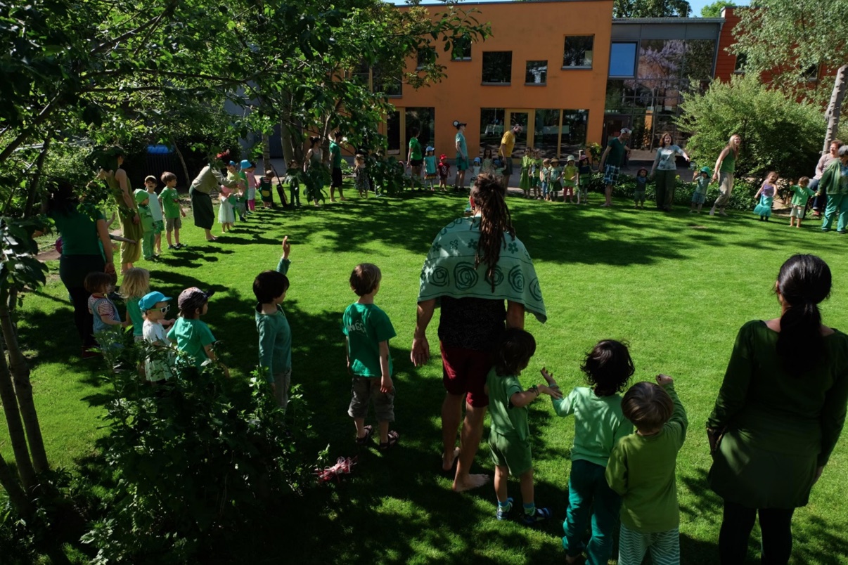 Kinder und Erzieher*innen im Kinderkreis im Garten vor dem Kinderhaus
