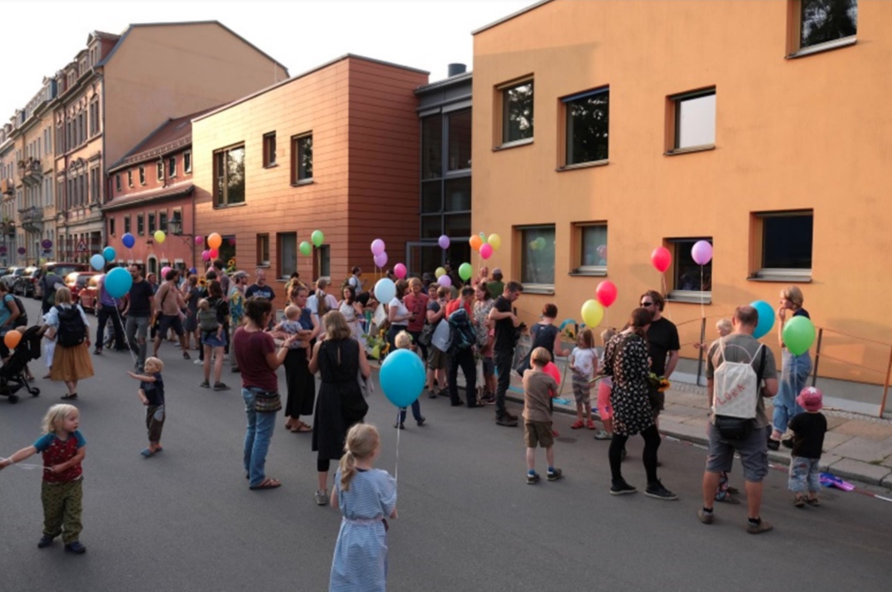 Familien mit bunten Luftballons beim Fest auf der Straße vor dem Kinderhaus
